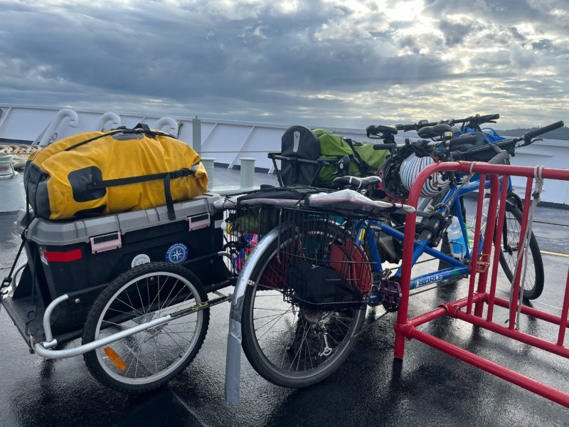 A tandem bicycle next to an e-bike with a trailer parked on a ferry deck.