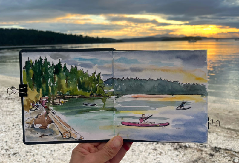 a hand holding a sketchbook with a sunset sketch in it.