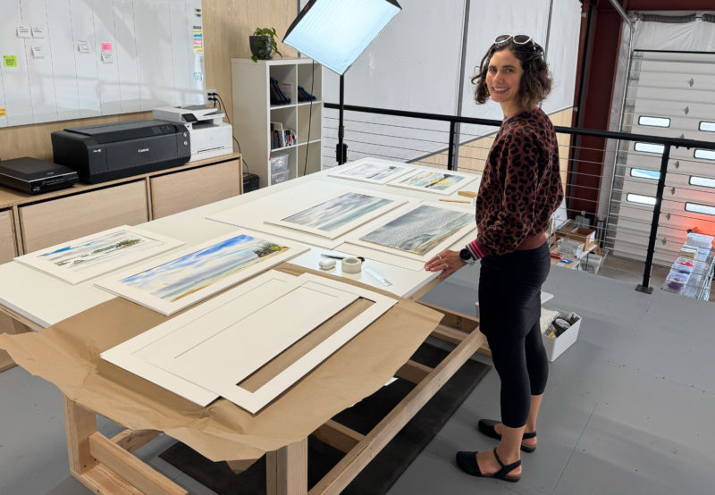 A woman stands at a large worktable with framing supplies on it.